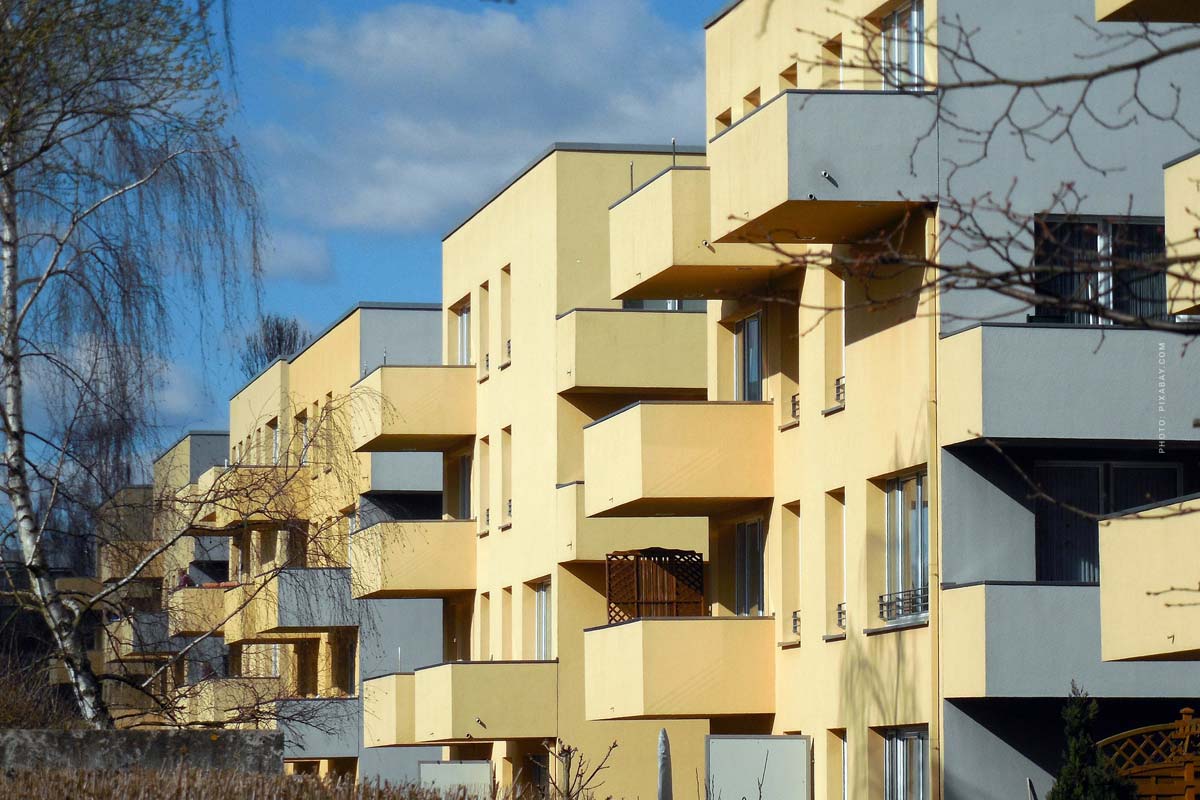 Mehrfamilienhaus mit gelb-weißer Fassade, modernen Fenstern und Balkonen im Neubau vor blauem Himmel